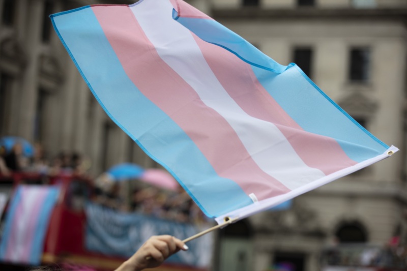 A large transgender pride flag being waved in the air.